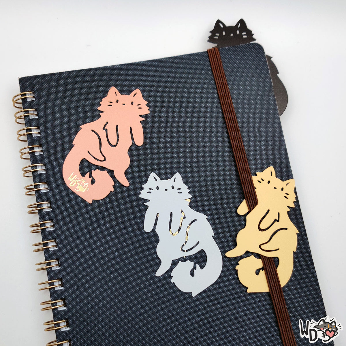 A Set of all four metal bookmarks sitting on top or attached to a small notebook